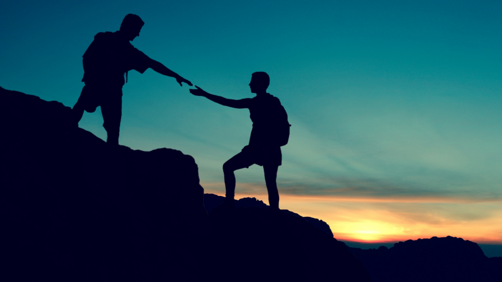 Silhouette of two climbers on a hillside, reaching out hands to offer each other support